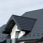A beautiful modern house is covered with black metal tiles. Roofing of metal profile wavy shape