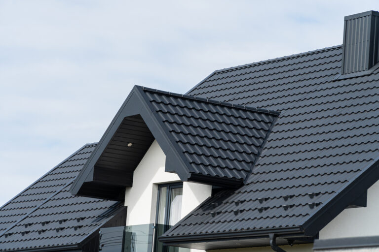A beautiful modern house is covered with black metal tiles. Roofing of metal profile wavy shape