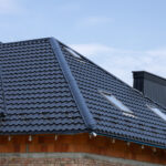 A modern home features a newly installed black tile roof with skylights under a bright blue sky, showcasing elegant design and craftsmanship
